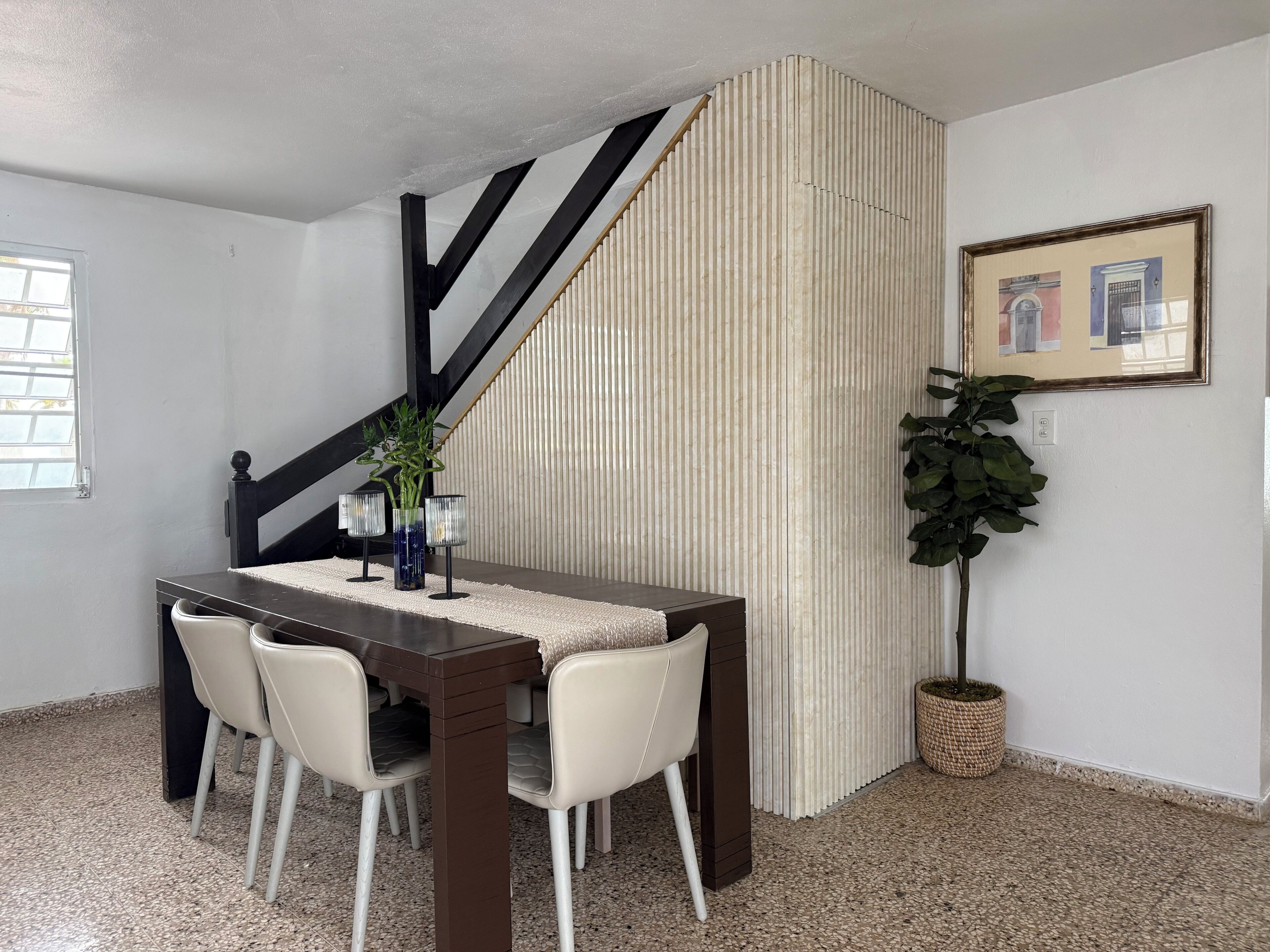 Un coin repas avec une table en bois foncé, des chaises blanches et un mur à rayures.
