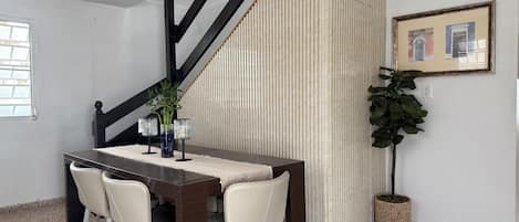 Un comedor con una mesa de madera oscura, sillas blancas y una pared a rayas.