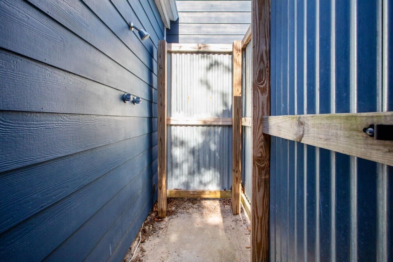 A narrow outdoor corridor with wooden siding and a corrugated metal fence.