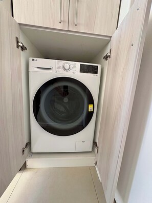 Een compacte, witte LG wasmachine met voorlader, geplaatst in een kast met een licht houten afwerking.