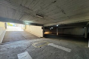 Garagem subterrânea com paredes de concreto, rampa metálica que leva a um acesso de rua e grelha de escoamento no chão.