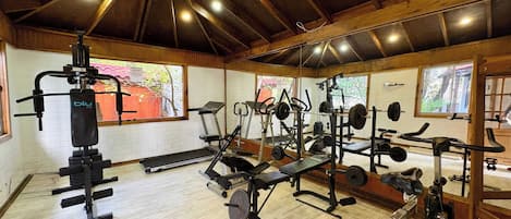 Un gimnasio con diversos equipos de ejercicio, vigas de madera en el techo y ventanas amplias.
