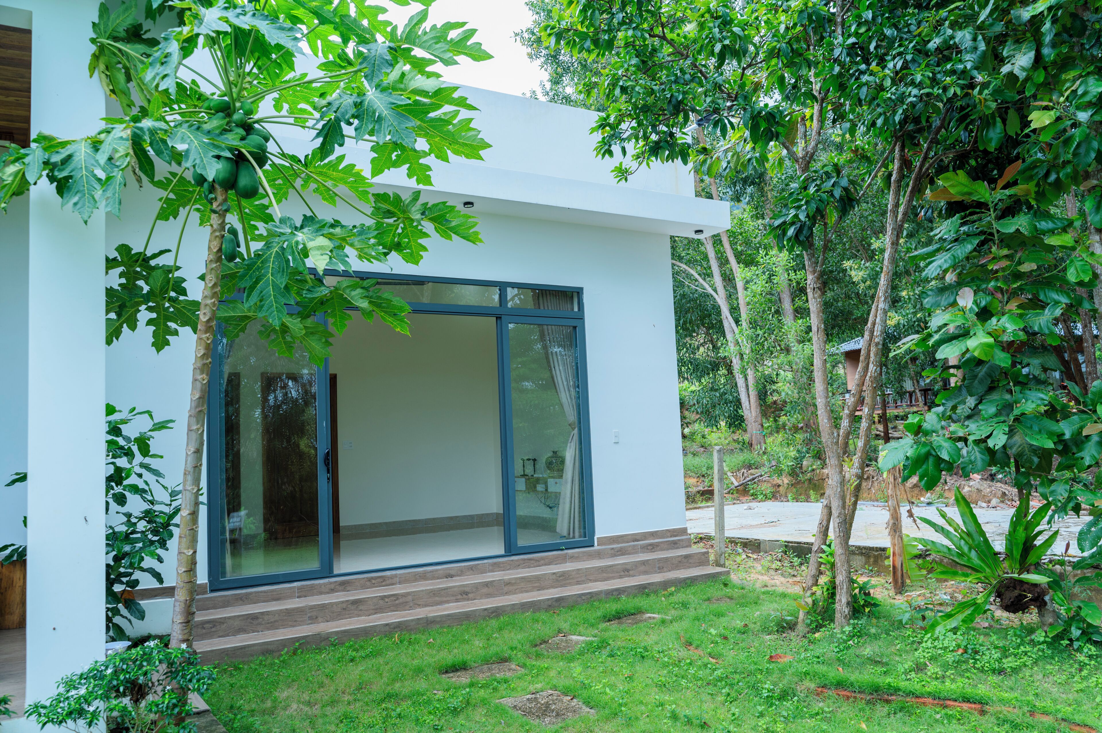 A modern house with a large glass door, surrounded by lush greenery.