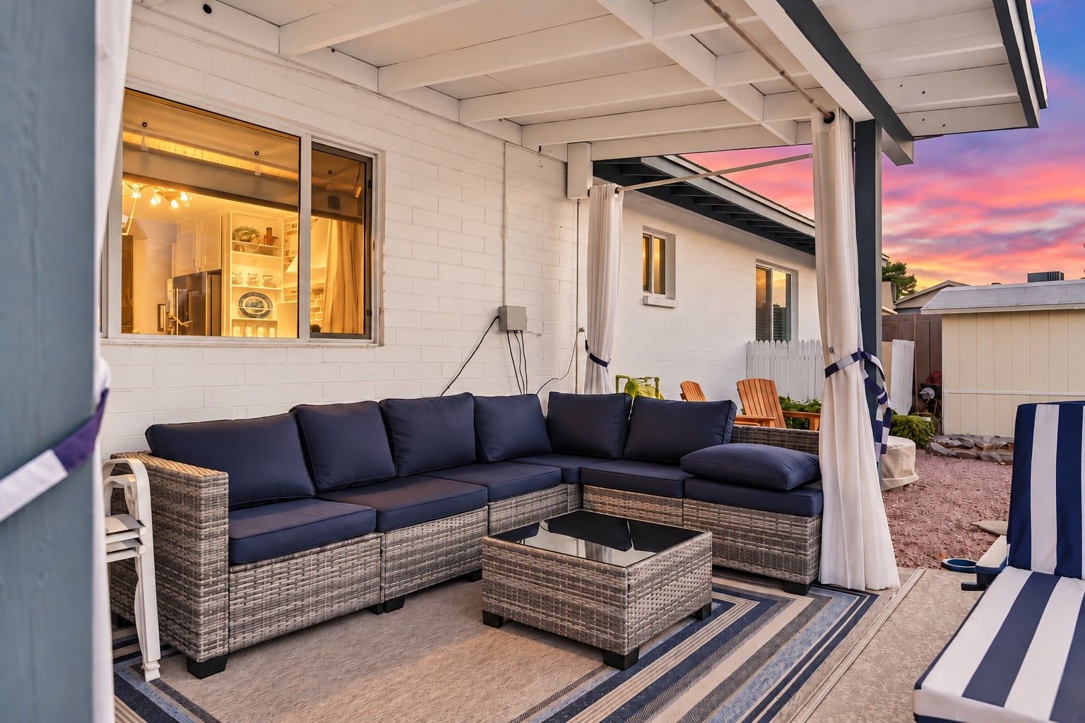 A covered outdoor seating area with a sectional sofa, a coffee table, and a lounge chair.