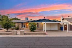 A two-story building with a garage, a small front yard with a tree, and a clear sky. - Campus Palms | Modern 3BR | Private Pool (Tempe)