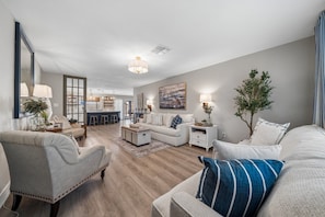 A modern living room with a sofa, armchairs, a coffee table, and a dining area with a kitchen in the background. - Campus Palms | Modern 3BR | Private Pool (Tempe)
