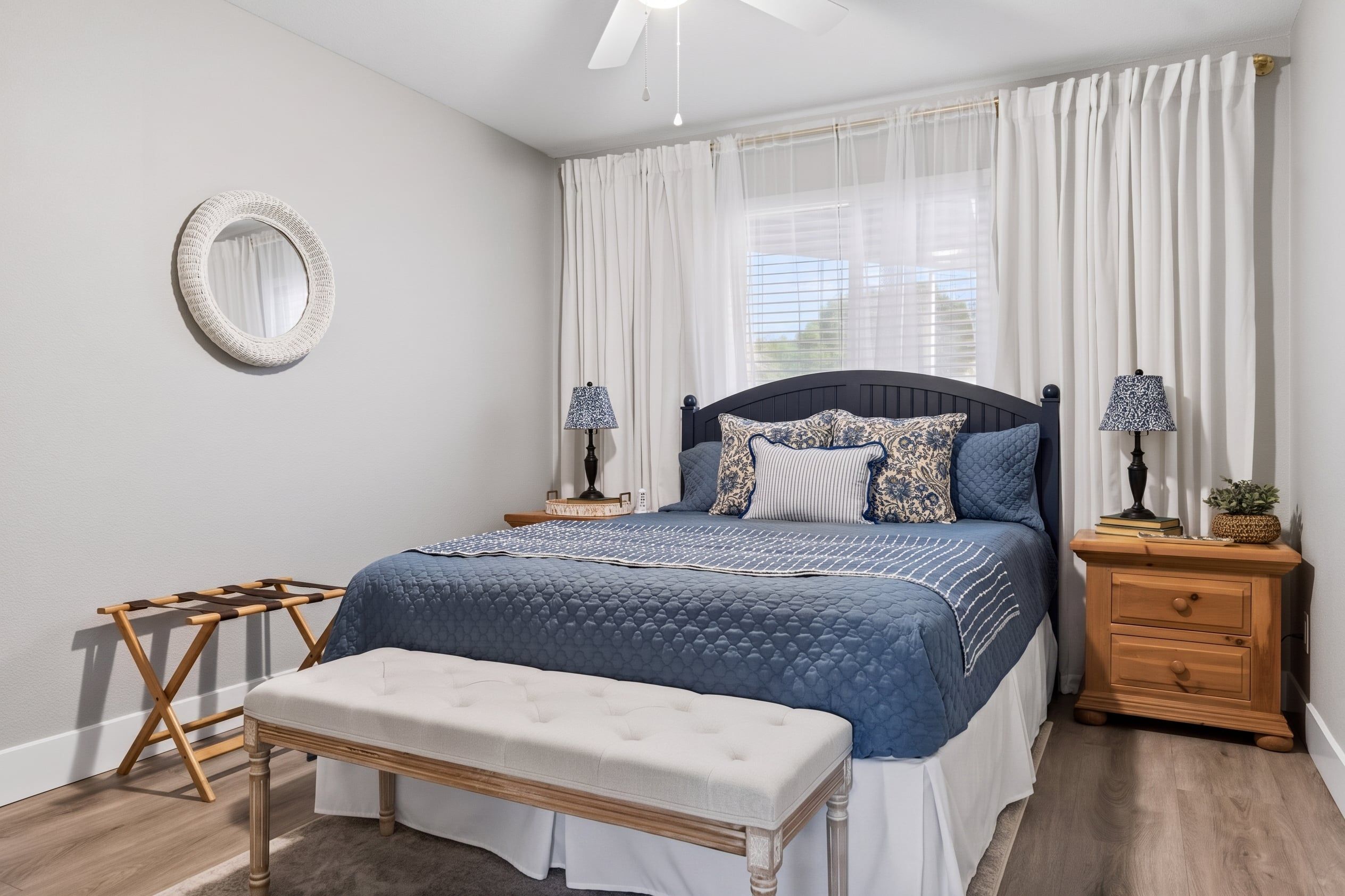 A bedroom with a bed, bedside tables, a bench, a mirror, and a ceiling fan.