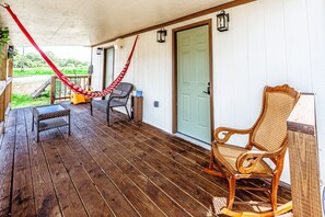A wooden porch with a hammock, wicker furniture, and a door.