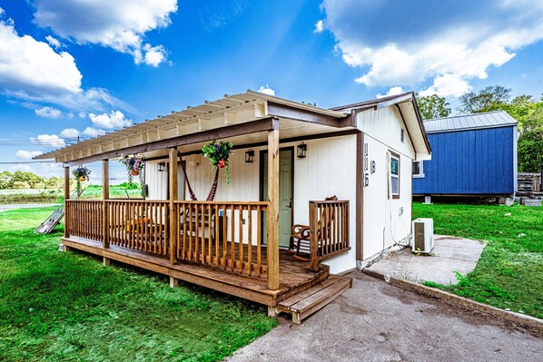 A small house with a wooden porch, a covered area, and a blue shed in the background.