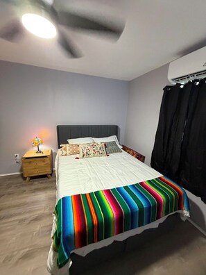A bedroom with a bed, a nightstand, a ceiling fan, and an air conditioning unit.