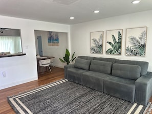 A modern living room with a grey sofa, a dining area with a table and chairs, and three framed botanical prints on the wall. - Pleasant 3-bedroom house with AC in charming Cocoa (Cocoa)
