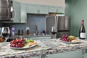 A kitchen with a marble countertop, two plates of food, a bottle of wine, and a toaster. - A vibrant 3BR retreat built for making memories together. (New Orleans)