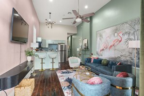A modern living room with a blue sofa, a white armchair, and a coffee table. There is a kitchen in the background with a refrigerator and a microwave. - A vibrant 3BR retreat built for making memories together. (New Orleans)