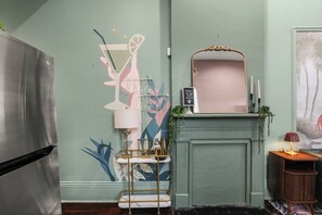 A room with a modern kitchen, a decorative wall with abstract art, a mirror with a gold frame, and a small table with candles. - A vibrant 3BR retreat built for making memories together. (New Orleans)