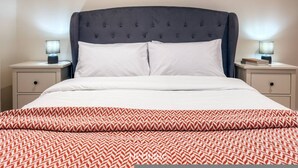 Un letto con testiera imbottita, due comodini con lampade e una coperta a motivi decorativi.