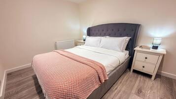 A bedroom with a bed, nightstands, a radiator, and a wooden floor.