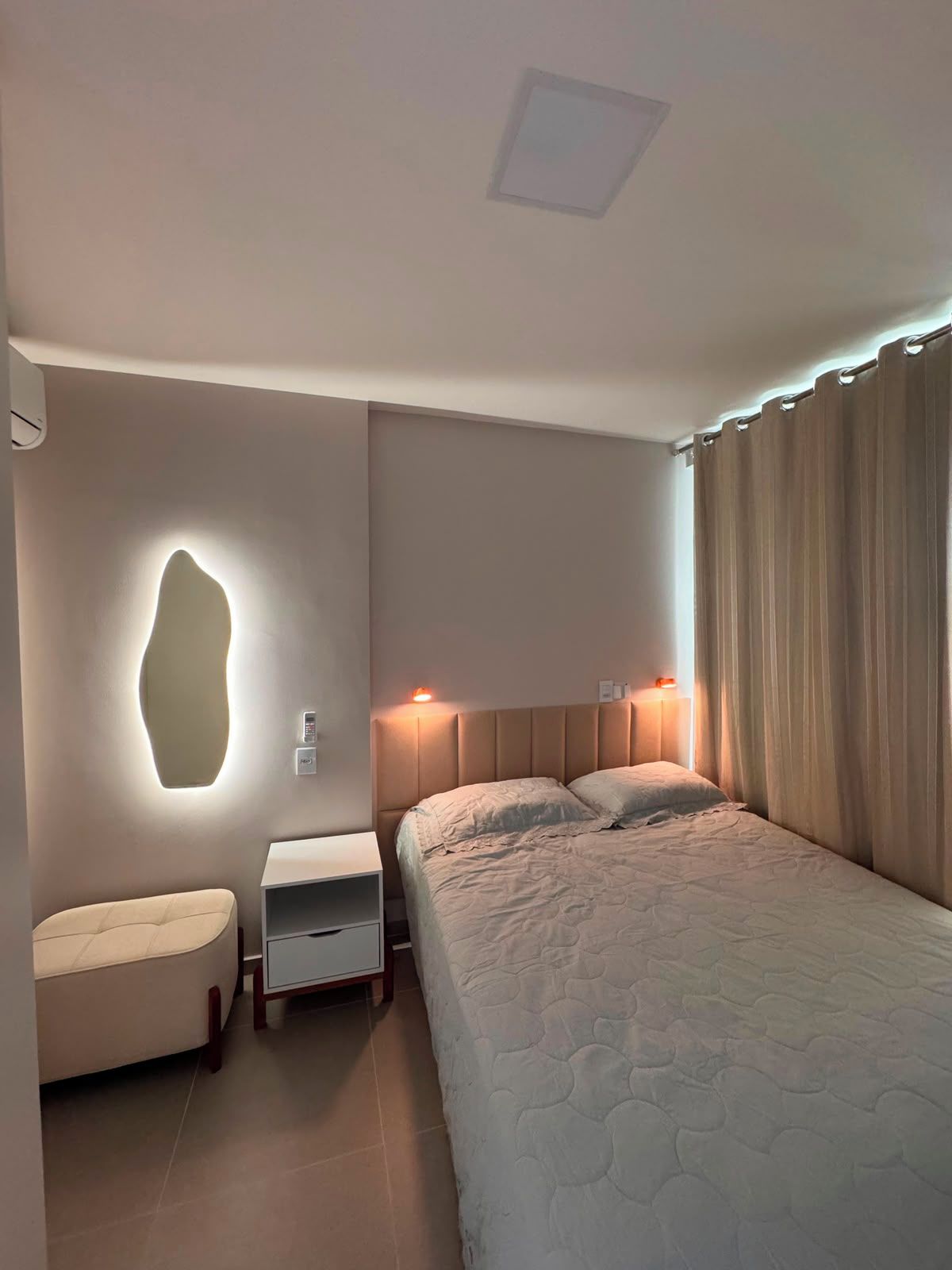 Ein Schlafzimmer mit einem Bett, Nachttischen, einer Wandlampe und einem Vorhang.