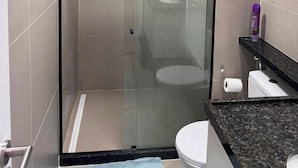 Een moderne badkamer met een douche met glazen wand, een toilet en een wastafel.