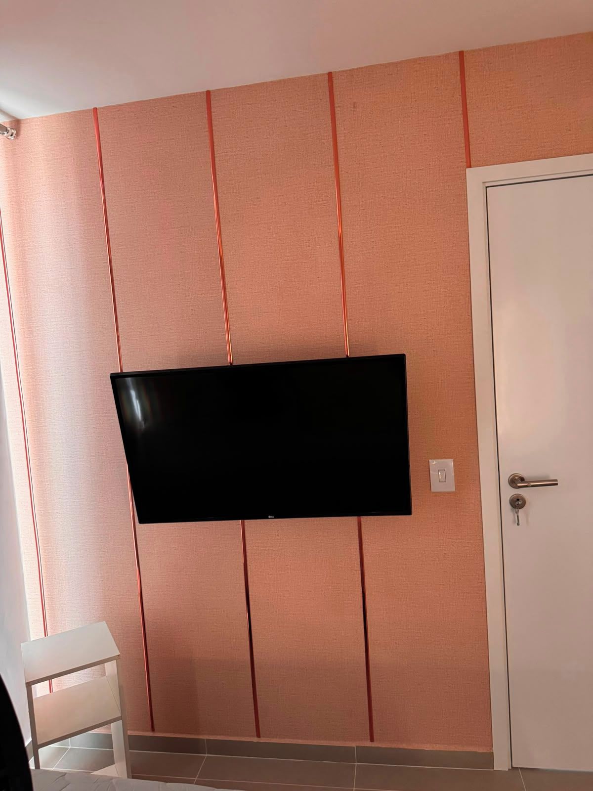 Une pièce avec un téléviseur fixé au mur, un mur à texture, une porte blanche et une petite table blanche.