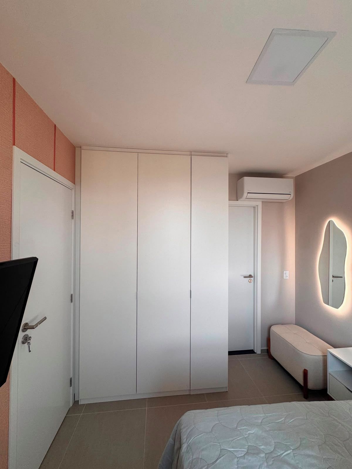Een slaapkamer met een bed, een kledingkast, een spiegel en een airconditioner.