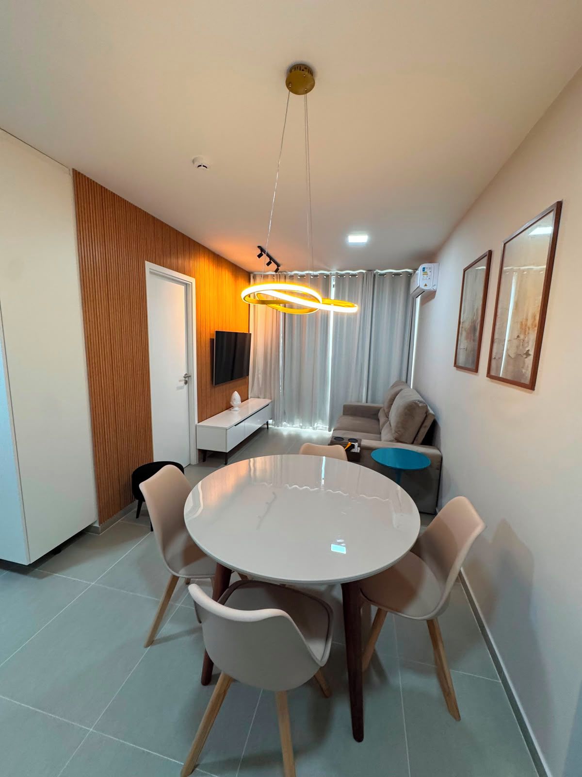 Een moderne woonkamer met een ronde eettafel, een bank, een televisie en een plafondlamp.