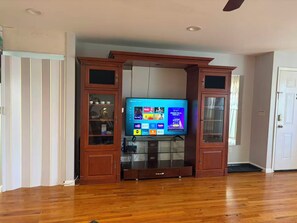 A living room with a wooden entertainment center housing a flat-screen TV, a fireplace, and a door leading to another room. - Large Duplex home near NYC and Staten island with Parking (Bayonne)