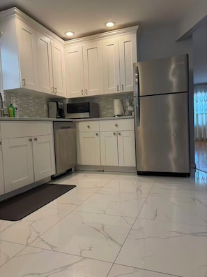 A modern kitchen with white cabinets, a stainless steel refrigerator, and a tiled floor. - Large Duplex home near NYC and Staten island with Parking (Bayonne)
