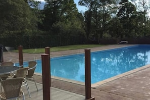 Una piscina con solárium de baldosas, rodeada de árboles y césped.