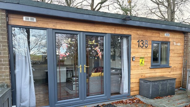 A modern building with large glass doors, a wooden exterior, and a number '138' on the wall. - Pet Friendly 2-Bed Lodge, Sleeps 5, Pool & Parking (Caernarfon)