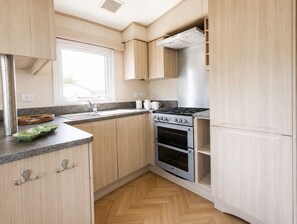 Una cucina compatta con mobili in legno, un fornello in acciaio inossidabile e una finestra che lascia entrare luce naturale.