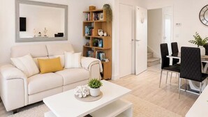 Uma sala de estar moderna com um sofá branco, uma mesa de centro e uma estante de livros.