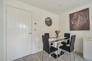 A dining area with a white table, black chairs, a vase with flowers, a wall clock, and a framed artwork.