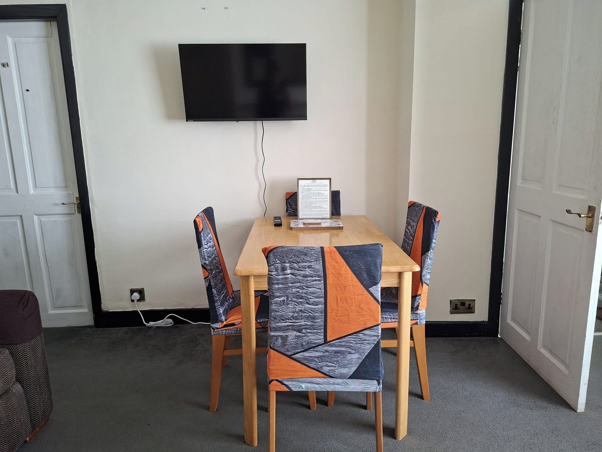 Una habitación con una televisión de pantalla plana montada en la pared, una mesa con sillas y un documento enmarcado sobre la mesa.