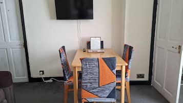 Una habitación con una televisión de pantalla plana montada en la pared, una mesa con sillas y un documento enmarcado sobre la mesa.