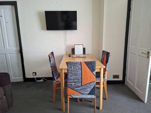 A room with a flat-screen TV mounted on the wall, a table with chairs, and a framed document on the table.