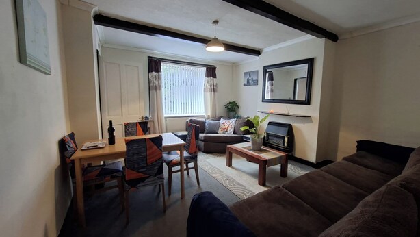 A living room with a brown sofa, a dining table with chairs, a small coffee table, and a fireplace. - Cosy Cottage Retreat in Huddersfield (Huddersfield)