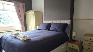 A bedroom with a bed, a nightstand, a dresser, and a window with curtains. - Cosy Cottage Retreat in Huddersfield (Huddersfield)