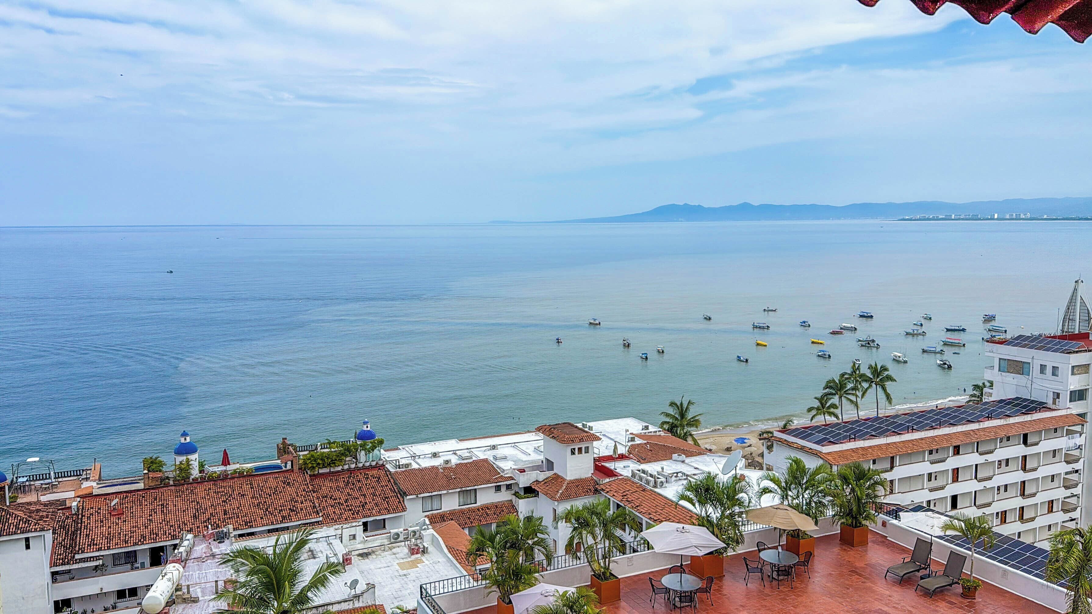 A coastal hotel with multiple balconies, a view of the sea, and several boats.