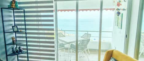 A room with a sliding glass door leading to a balcony with a view of the sea.