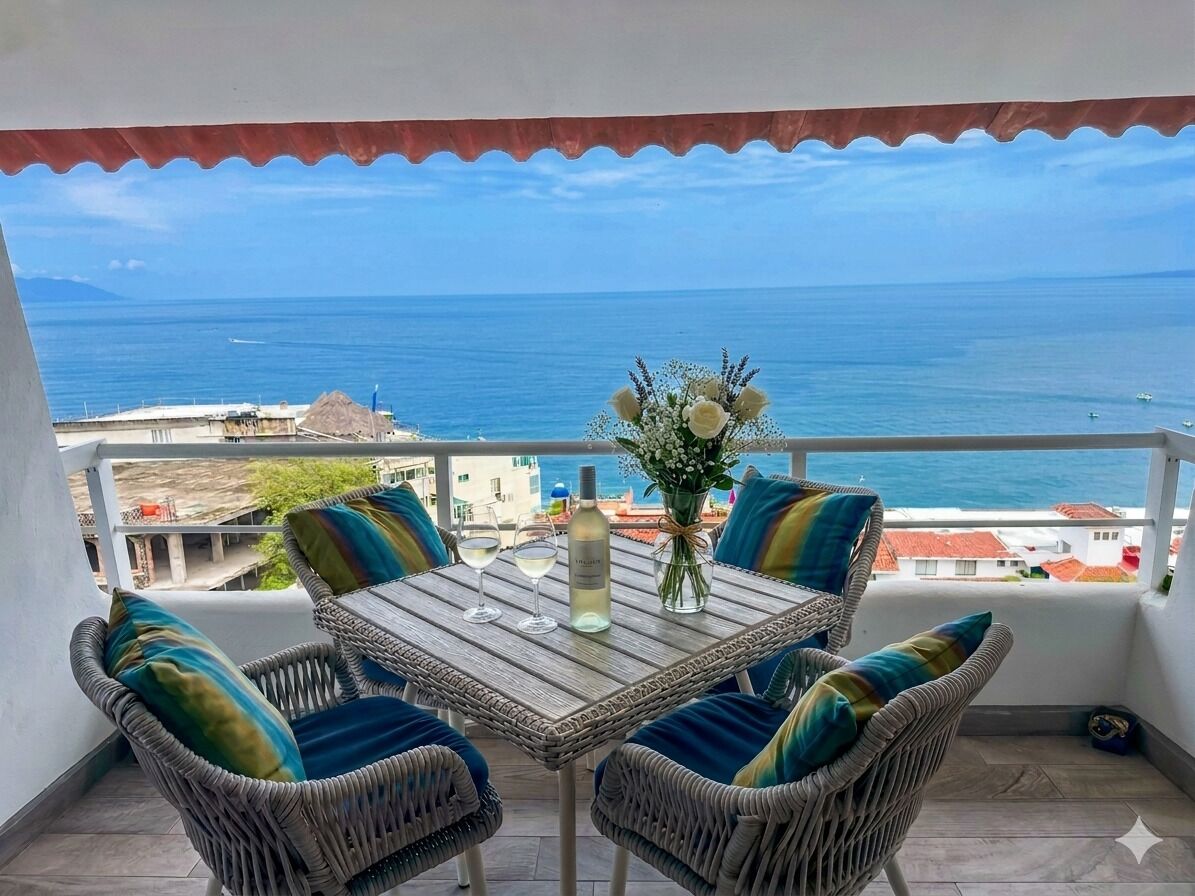 A balcony with wicker furniture, a table with a vase of flowers, and a view of the sea.