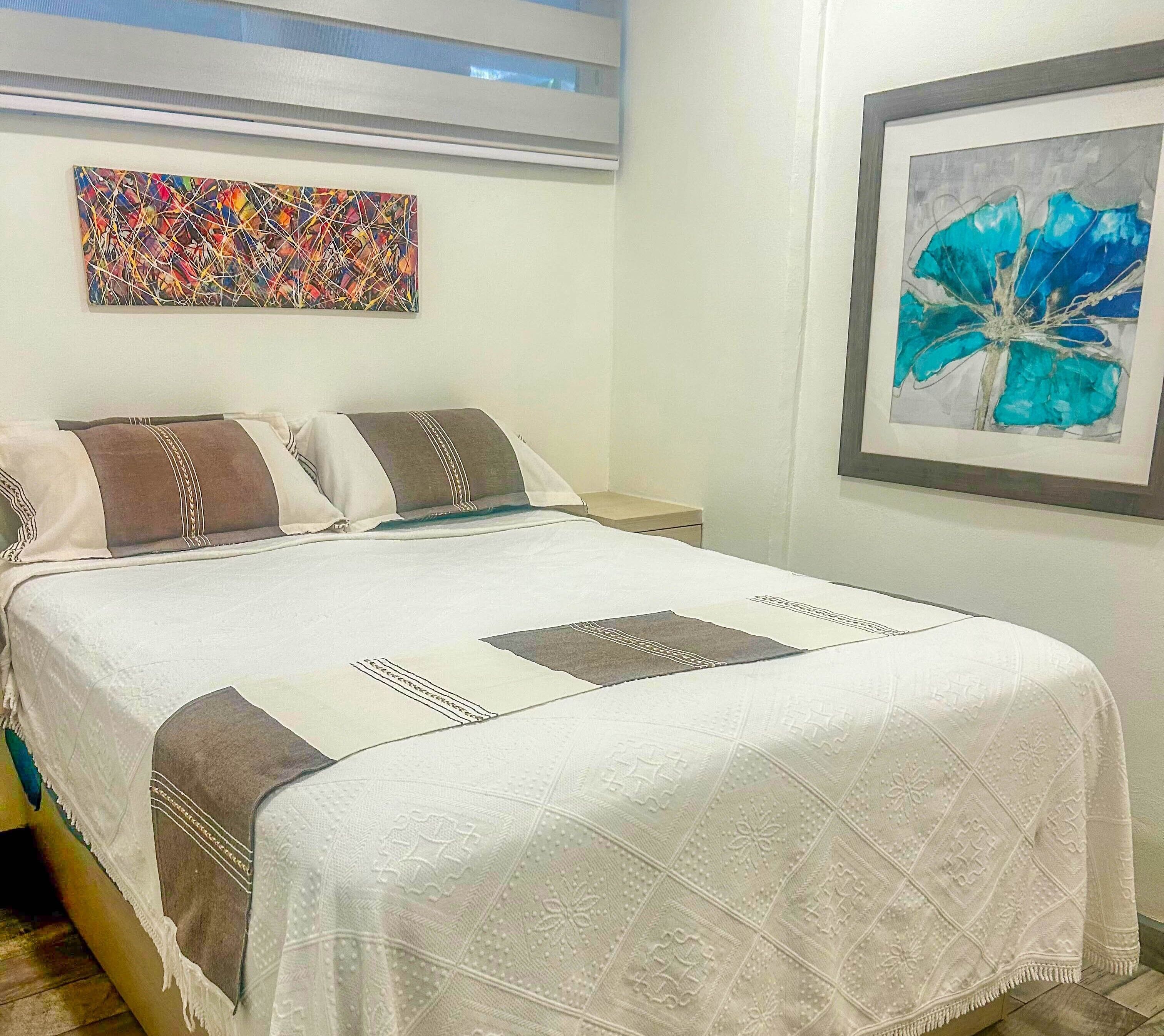 Una cama bien hecha con un edredón estampado, dos almohadas y una mesita de noche con una lámpara.