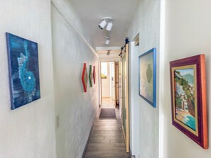 A hallway with artwork on the walls, a wooden floor, and a ceiling-mounted light fixture. - Boana Torre Malibu #803 , Ocean view, romantic zone (Puerto Vallarta)