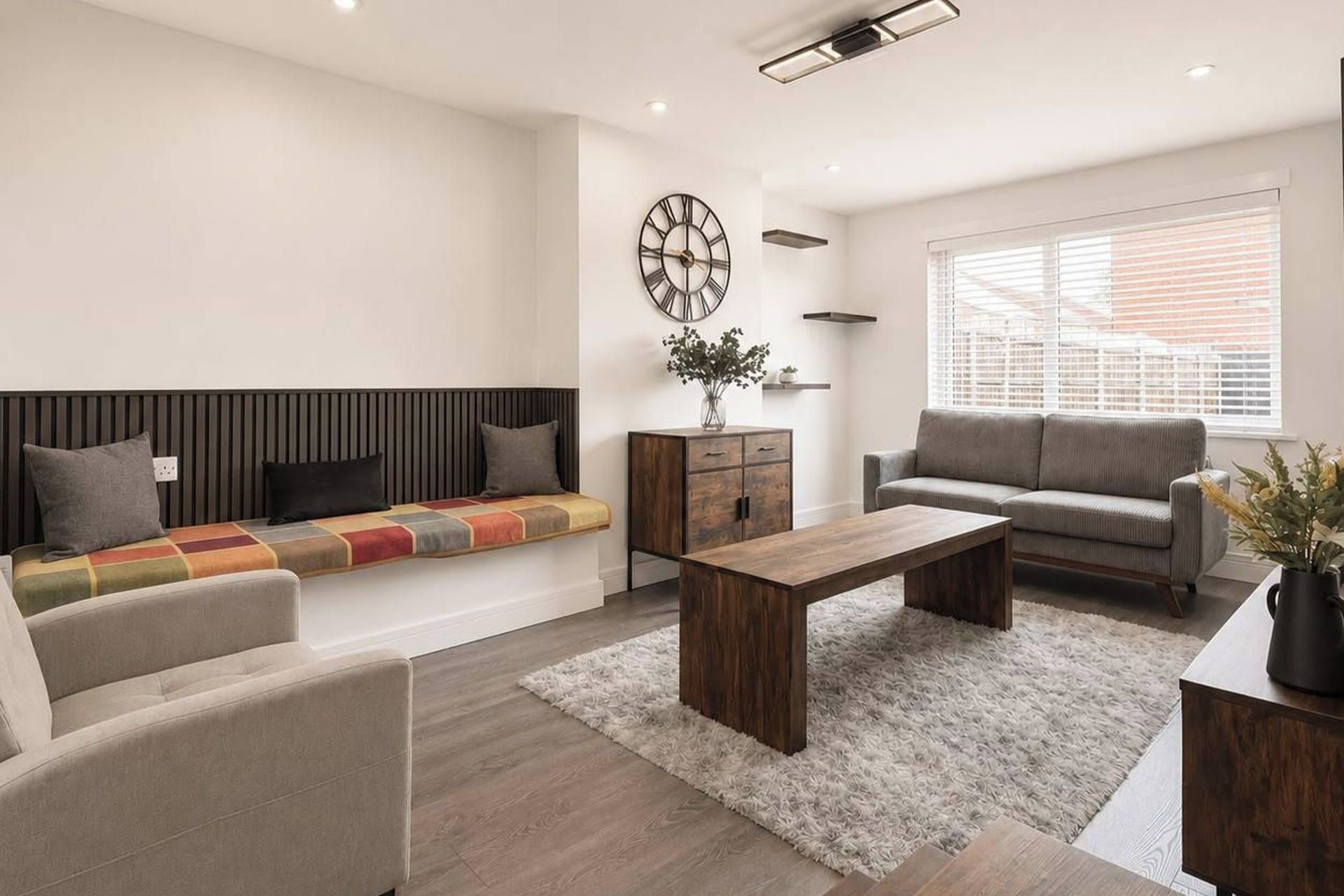 Un salon moderne avec un canapé, une table basse, une table d’appoint et une fenêtre équipée de stores.