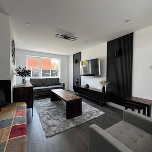 A modern living room with a sofa, coffee table, and TV against a wall. - The Cozy home - Cozy 3 Bedroom House (Telford)