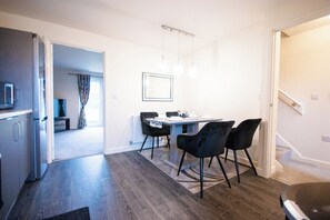 A modern kitchen with a built-in oven, a dining area with a table and chairs, and a staircase leading to another level. - Cozy Coventry Retreat - 3 Bedroom House (Coventry)
