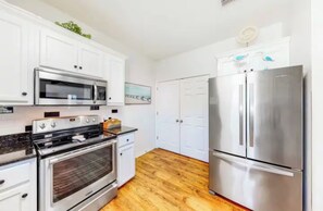A kitchen with white cabinets, a stainless steel refrigerator, a microwave, and a stove. - White Sands Beach House Sleeps 10 with Pool (Gulf Shores)