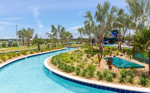 A swimming pool with a curved design, surrounded by palm trees and a water slide. - Renovated 4 BDR With pvt Pool (Kissimmee)