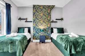 Une chambre d’hôtel avec deux lits, une table de chevet, une étagère fixée au mur et une fenêtre avec des rideaux.