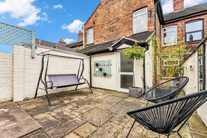 A courtyard with a swing set, a potted plant, and a black chair. - Spacious Stoke Townhouse 3Br Near Hospital (Stoke-on-Trent)