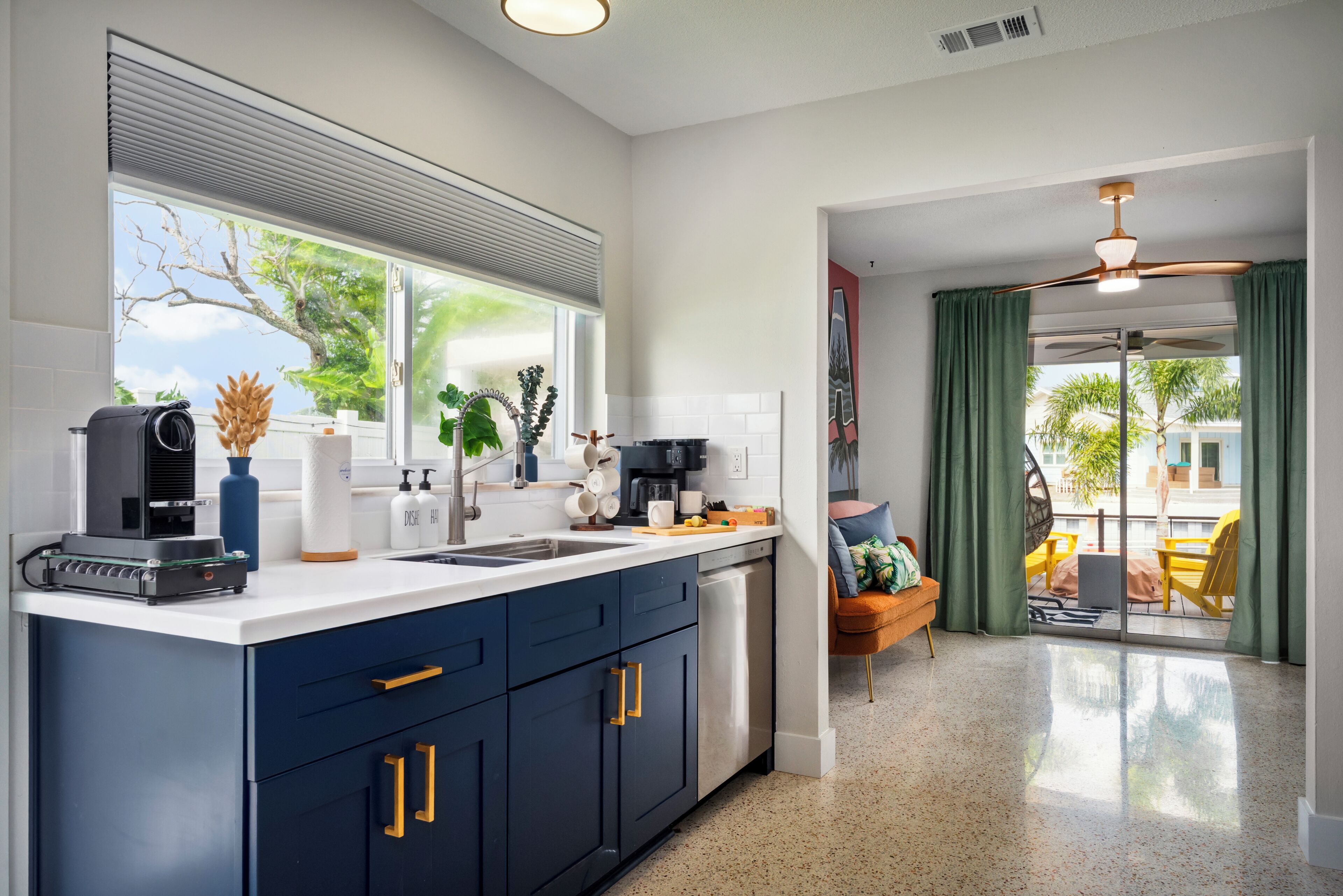 A modern kitchen with a large window, a dishwasher, and a dining area with a yellow chair.